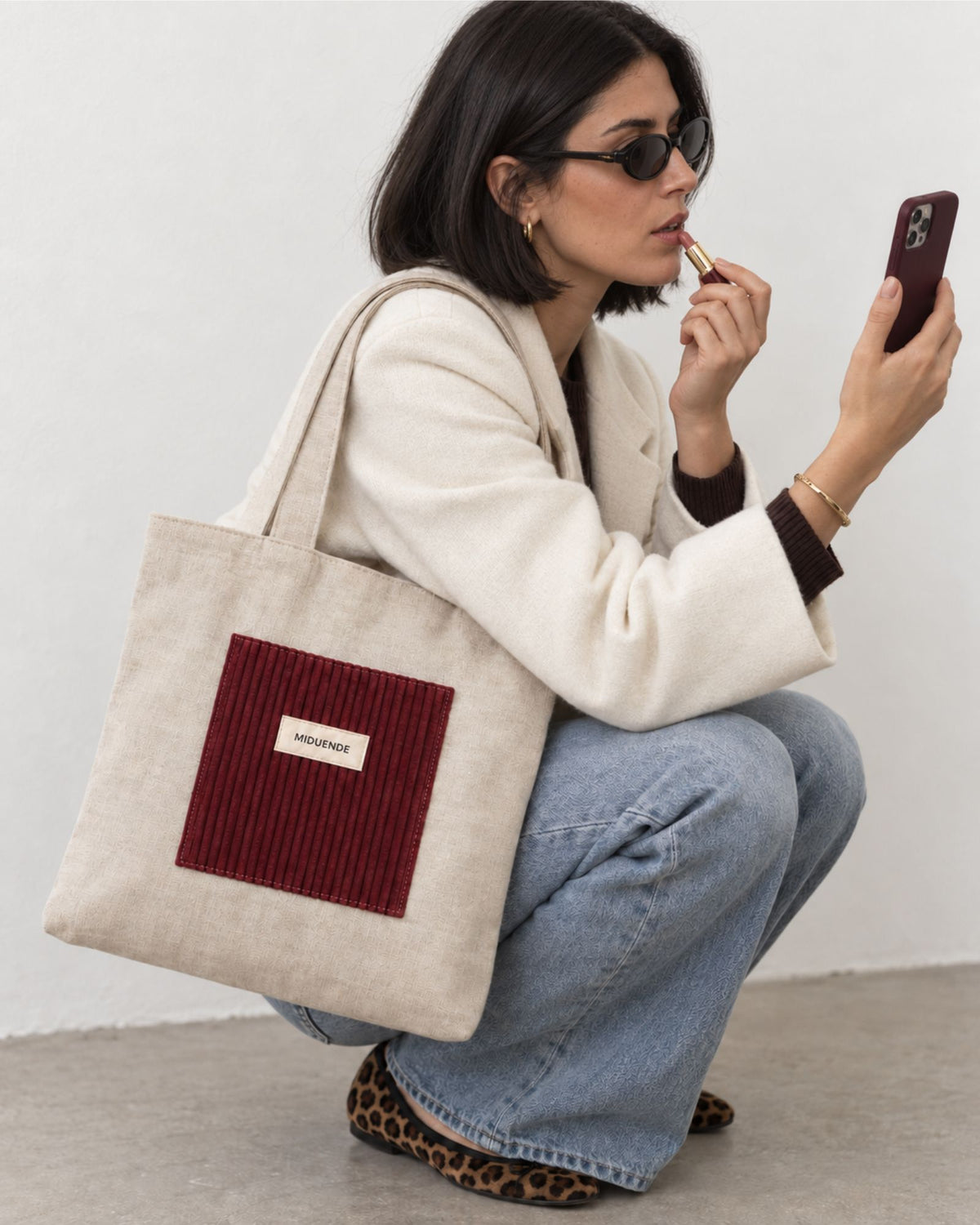 Modelo con Bolso Tote de lino con bolsilloesterior de pana color vino, asas cortas e interior acolchado.